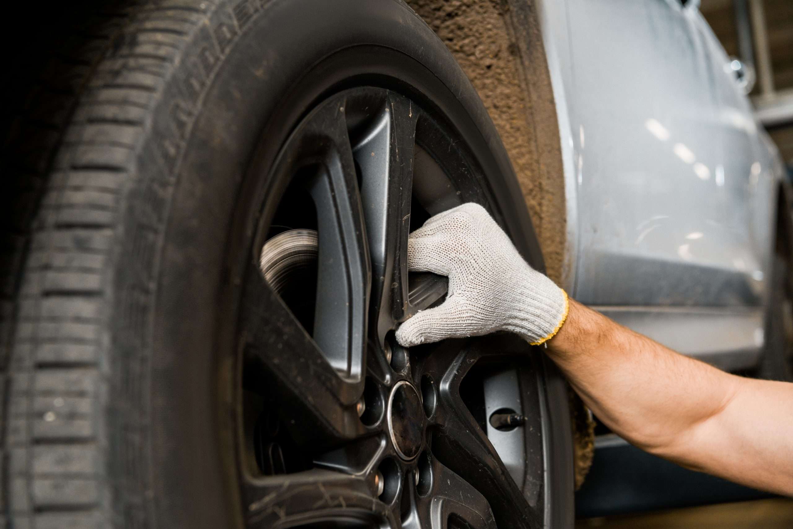 cropped shot of repairman in protective glove examining car wheel at auto repair shop
